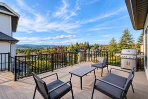 Una terraza con mobiliario exterior, una parrilla y una vista panorámica de una zona residencial.