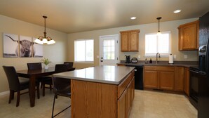 Una cocina moderna con armarios de madera, una isla central y una zona de comedor con sillas y una mesa.
