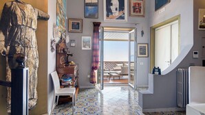 A room with a patterned floor, a wooden cabinet, a white chair, and a view through an open door to an outdoor area.