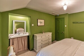 Une chambre à coucher comprenant un lit, une commode, une coiffeuse avec un miroir et une porte.