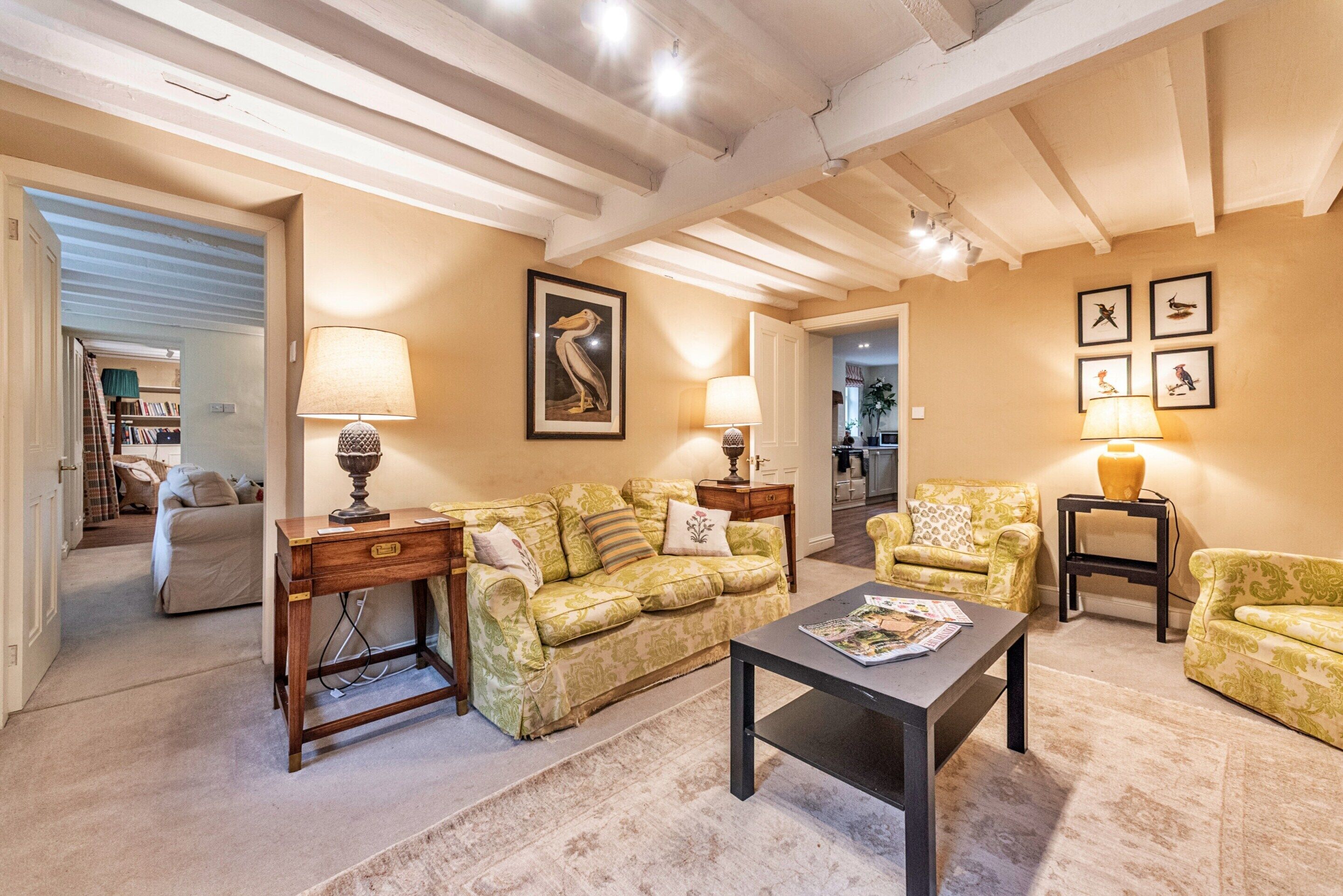 A living room with a sofa, a coffee table, and a lamp. There is a framed picture on the wall and a door leading to another room.