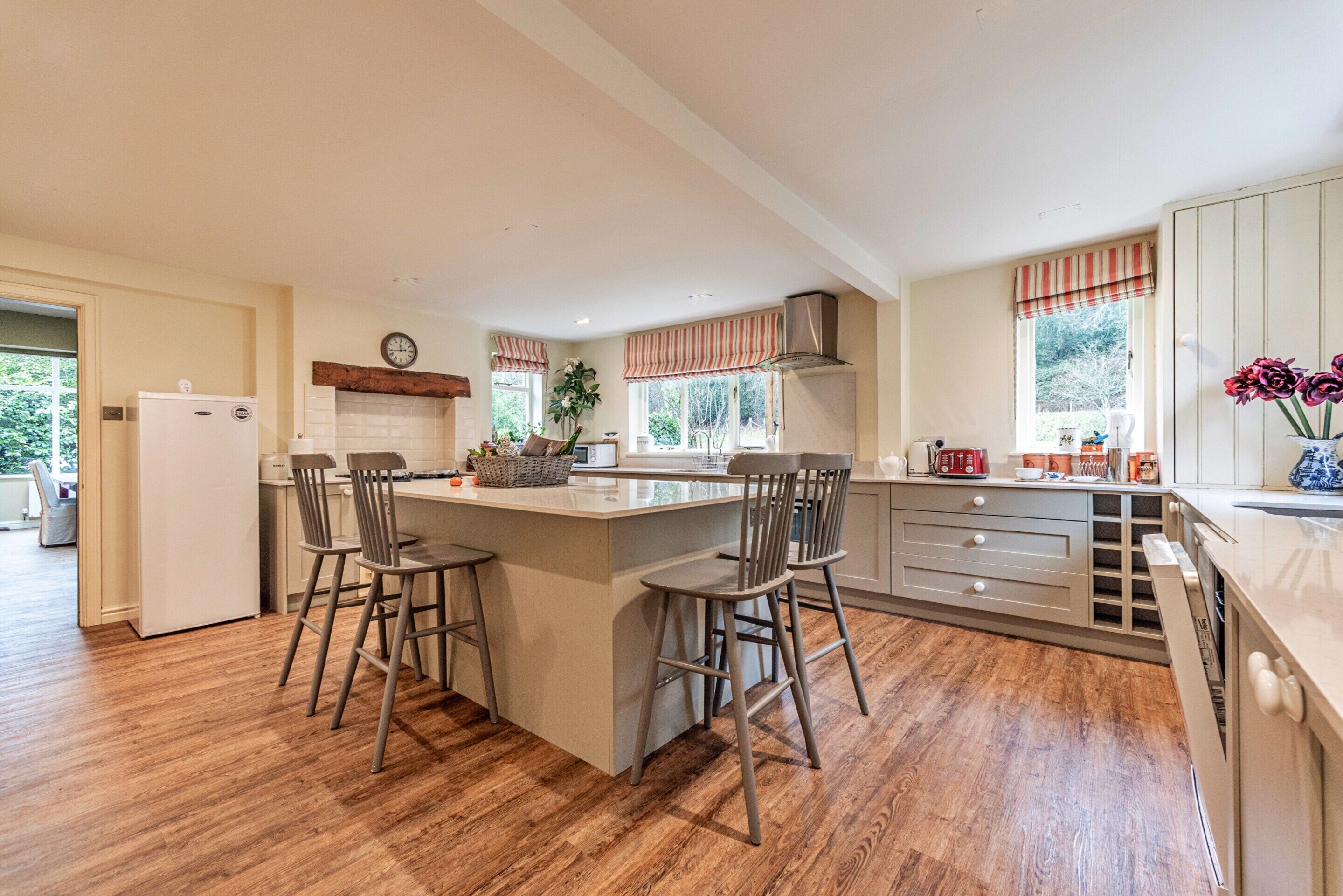 A modern kitchen with a central island, bar stools, a refrigerator, and a window with striped curtains.