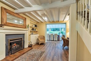 A spacious living room with a fireplace, wooden flooring, and a view through a large window. - Spacious Cottage Near Denbigh (Denbigh)