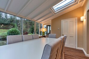 A room with a long table, seating, a door, and a window with a view of greenery. - Spacious Cottage Near Denbigh (Denbigh)