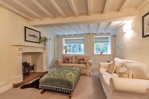 A cozy living room with a fireplace, two sofas, a green patterned ottoman, and a window with a view of trees. - Spacious Cottage Near Denbigh (Denbigh)