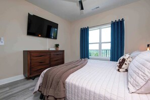 Ein Schlafzimmer mit Bett, Kommode, Wandfernseher und einem Vorhangfenster.