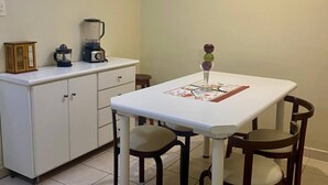 Un pequeño comedor con una mesa blanca, cuatro sillas, un ventilador de techo y una encimera de cocina con electrodomésticos.