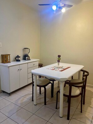 A small dining area with a white table, four chairs, a ceiling fan, and a kitchen counter with appliances. - Apartment in Guaruja Enseada (300m from the sea) (Guarujá)
