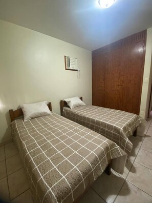 A room with two beds, a wooden wardrobe, and a wall-mounted thermostat. - Apartment in Guaruja Enseada (300m from the sea) (Guarujá)