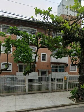 A residential building with a brick facade, white window frames, and a white metal fence. - Apartment in Guaruja Enseada (300m from the sea) (Guarujá)