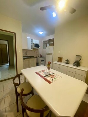 A kitchen with a central island, two chairs, a refrigerator, a stove, and a microwave. - Apartment in Guaruja Enseada (300m from the sea) (Guarujá)