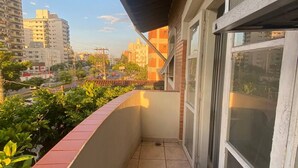 Un balcón con piso de baldosas, pared de ladrillo rojo y vista de un paisaje urbano con edificios y cielo despejado.