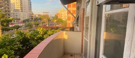 A balcony with a tiled floor, a red brick wall, and a view of a cityscape with buildings and a clear sky.