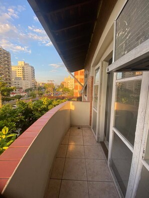 A balcony with a tiled floor, a red brick wall, and a view of a cityscape with buildings and a clear sky. - Apartment in Guaruja Enseada (300m from the sea) (Guarujá)