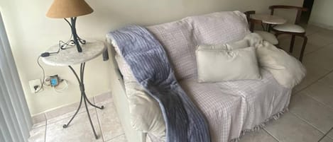 Una sala de estar con un sofá, una mesita con una lámpara y un cuadro colgado en la pared.