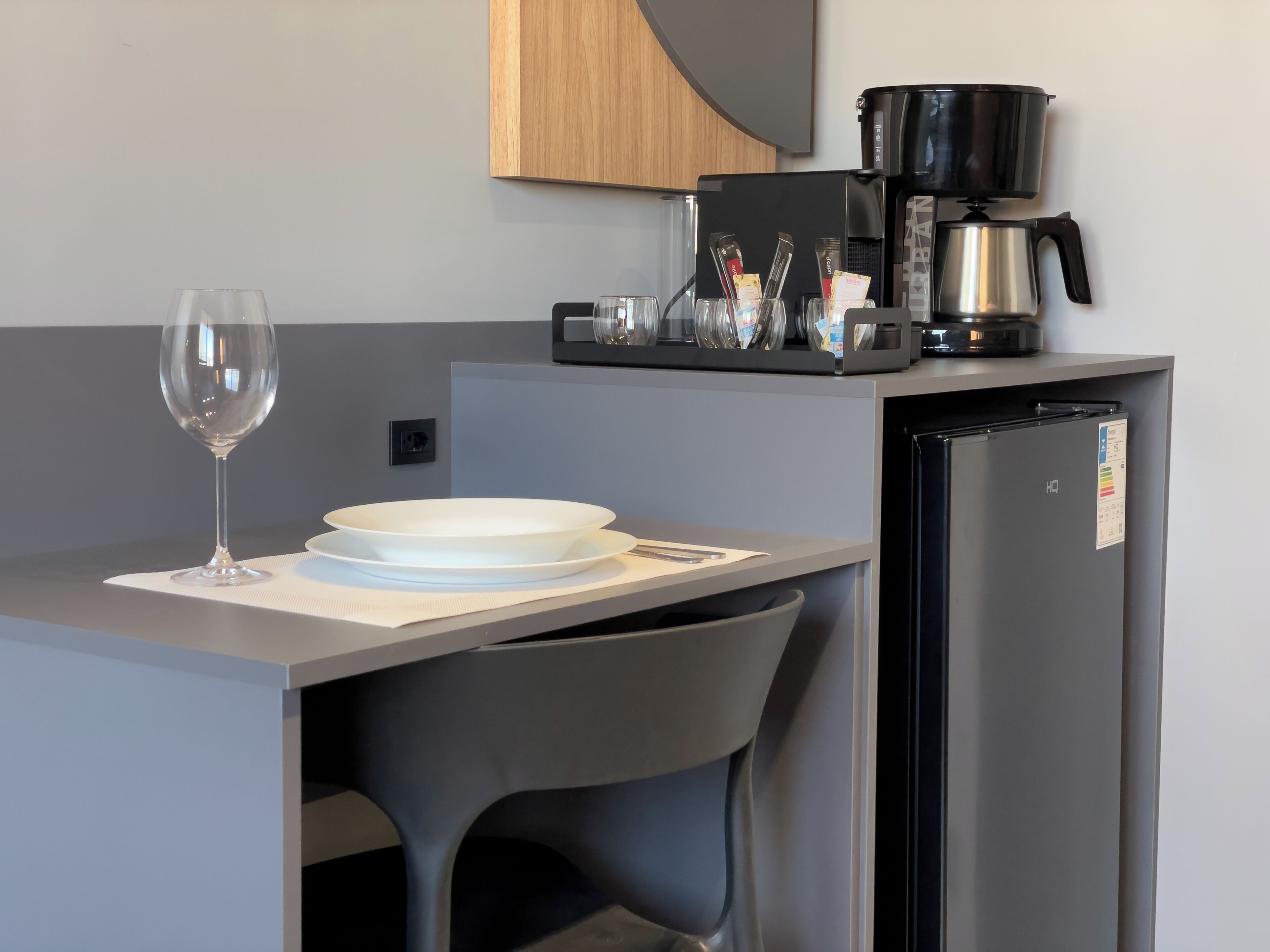 Uma cozinha compacta com cafeteira, geladeira, um copo de vinho e um prato sobre a mesa.