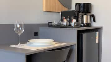 Uma cozinha compacta com cafeteira, geladeira, um copo de vinho e um prato sobre a mesa.