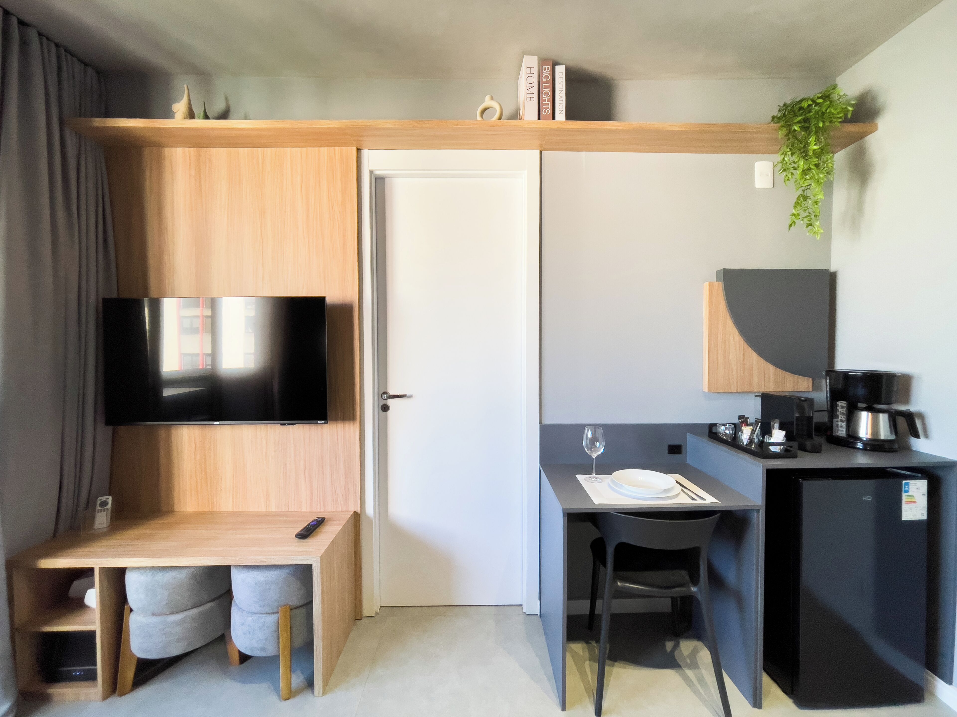Una habitación compacta con televisión, escritorio con silla, refrigerador pequeño y cafetera.