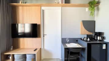 Una habitación compacta con televisión, escritorio con silla, refrigerador pequeño y cafetera.