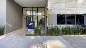 Entrada de un edificio moderno con un letrero Nex One, un bolardo de seguridad y el número 48.