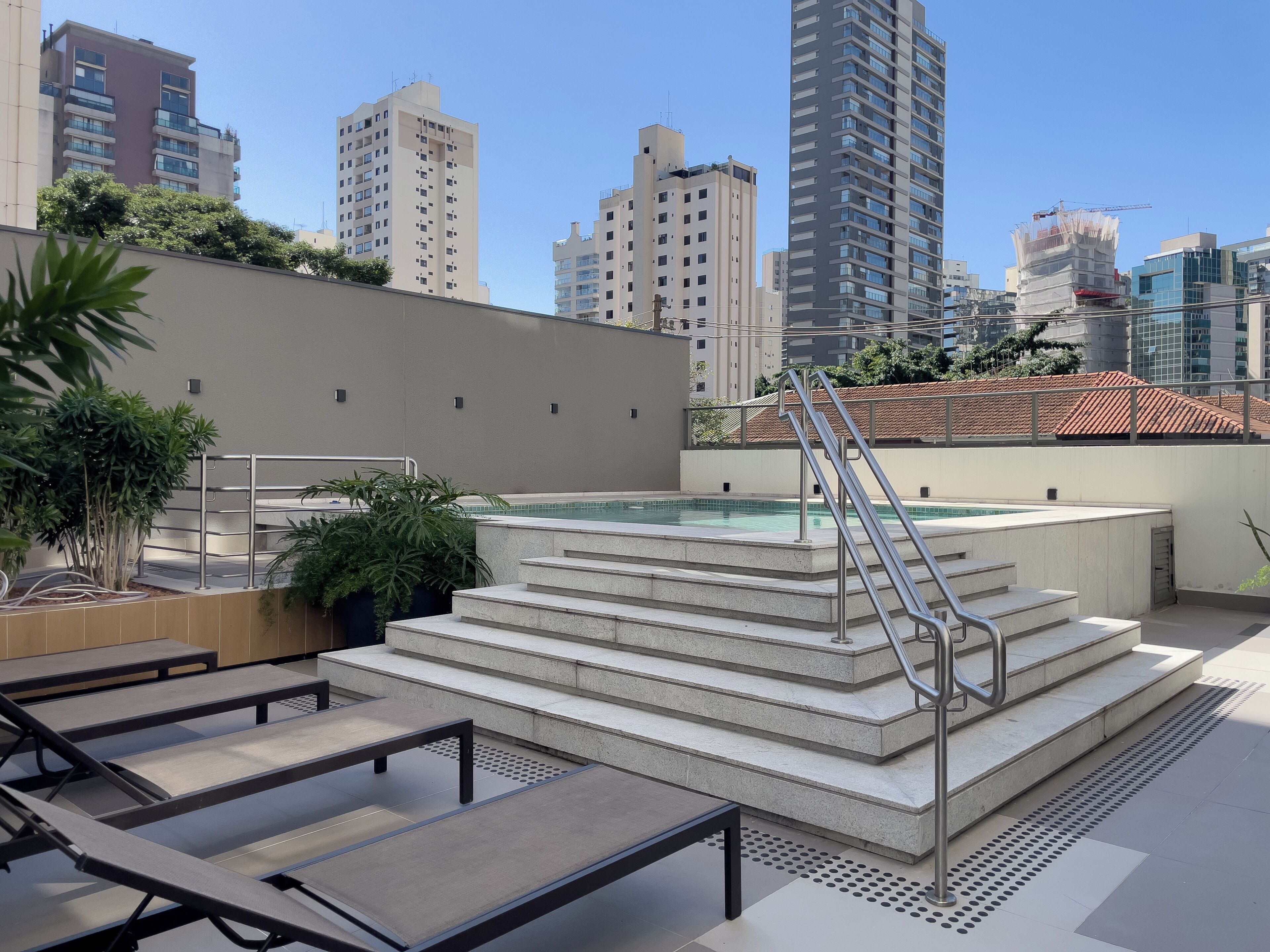 Un área de piscina en la azotea con escalones que bajan al agua, rodeada de edificios modernos.