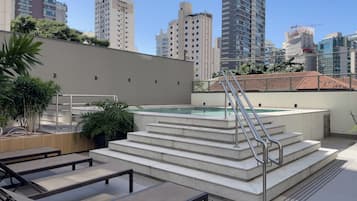 Un área de piscina en la azotea con escalones que bajan al agua, rodeada de edificios modernos.