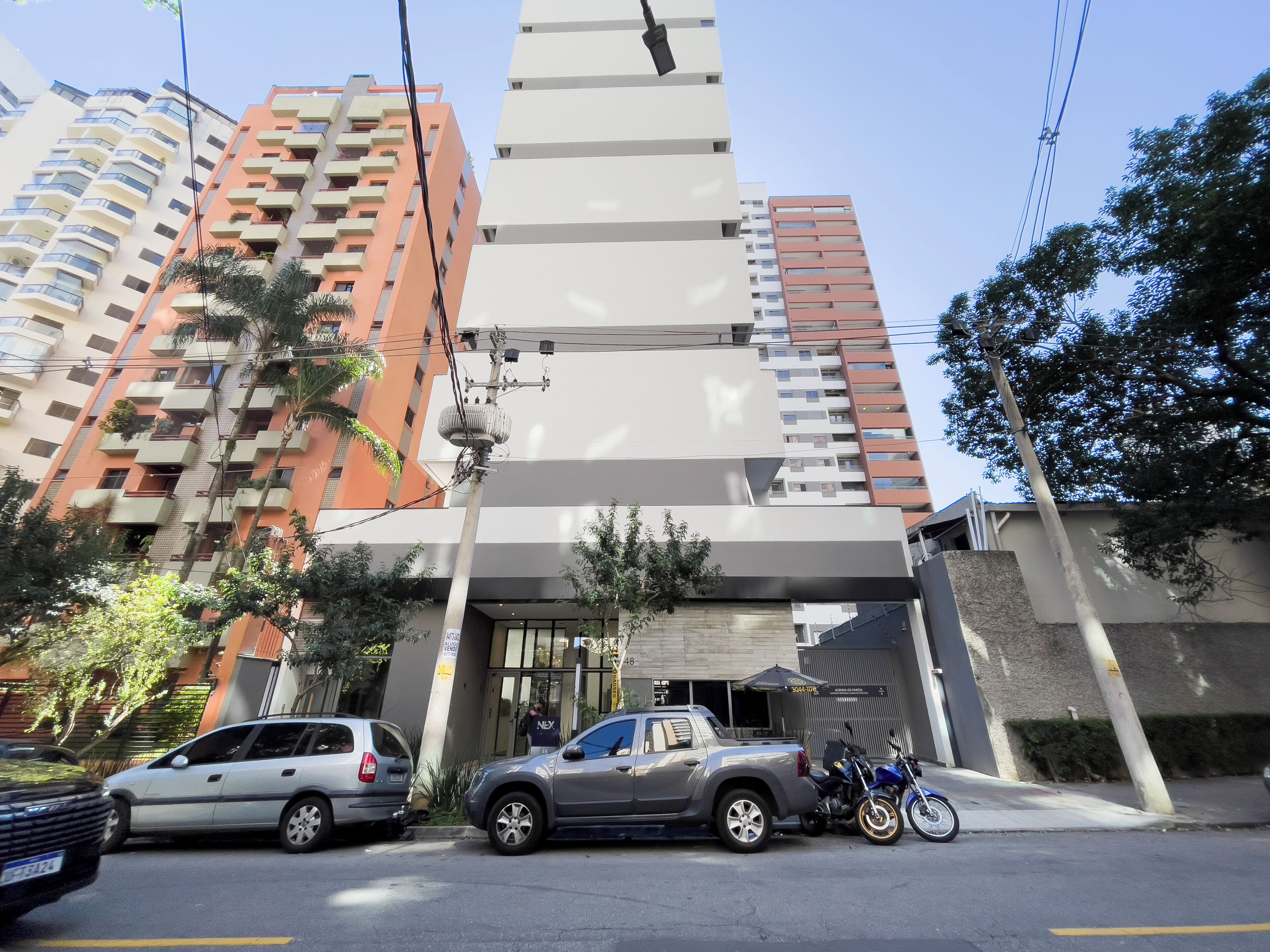 Edifício de vários andares com design moderno, destacando uma entrada imponente com porta de vidro e uma pequena cobertura.