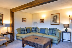 Una sala de estar acogedora con techo de vigas de madera, un sofá verde con cojines escoceses, una mesa de centro de madera y cuadros en las paredes.