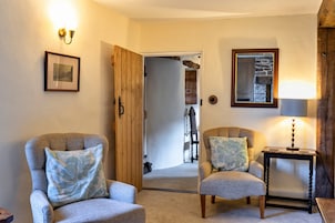 Una sala acogedora con dos sillones, una mesita con una lámpara y una puerta de madera que da a otra habitación.