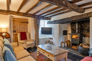 A cozy living room with a fireplace, wooden beams, a sofa, and a television. - Luxury Cotswolds Cottage for 7 (Okehampton)