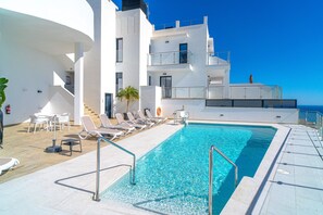 Ein Swimmingpool mit Liegestühlen und einer Palme, umgeben von einem weißen Gebäude mit Balkonen.