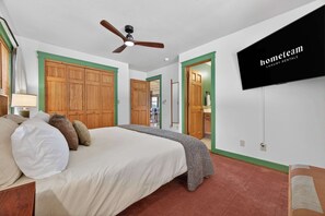 Ein Schlafzimmer mit einem Bett, einem Deckenventilator, einem an der Wand befestigten Fernseher und einer grün gerahmten Tür.