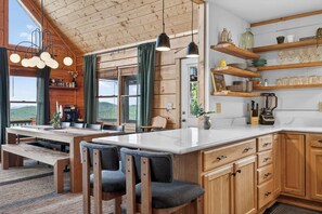 Ein Holzblockhaus-Interieur mit Essbereich, Küche und Regalen mit Gläsern.