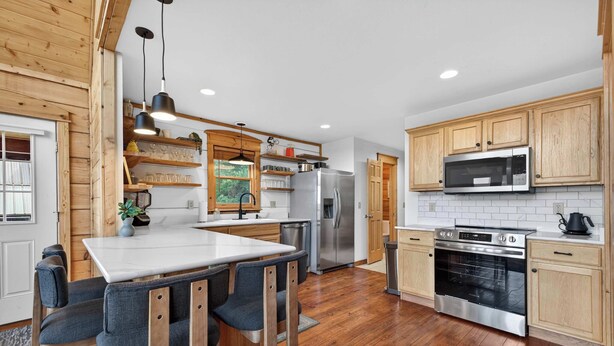 A modern kitchen with wooden cabinets, stainless steel appliances, and a central island with bar stools. - Ski-Out to Hatley Pointe • Alpine Slide • Rec Room (Mars Hill)
