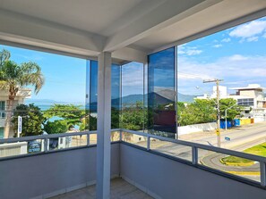 Un balcón con vista a una calle y follaje, cielo despejado, y un edificio con reflejo en el vidrio.