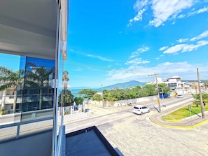 A view from a window overlooking a street with a white car, a pedestrian crossing, and a clear blue sky. - Canto Grande by LikeHome (Bombinhas)