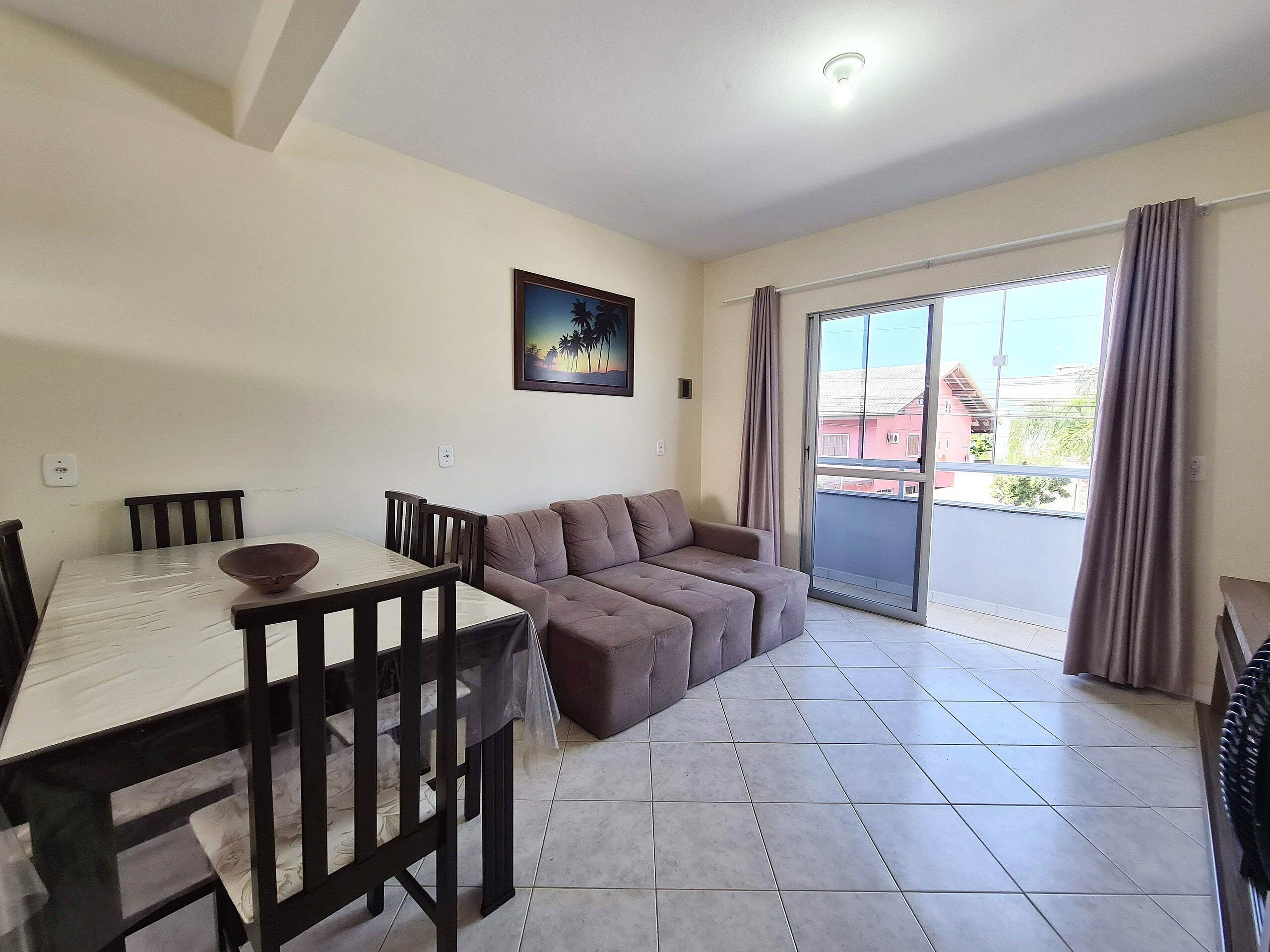 A living room with a dining table, chairs, a sofa, and a sliding glass door leading to a balcony.