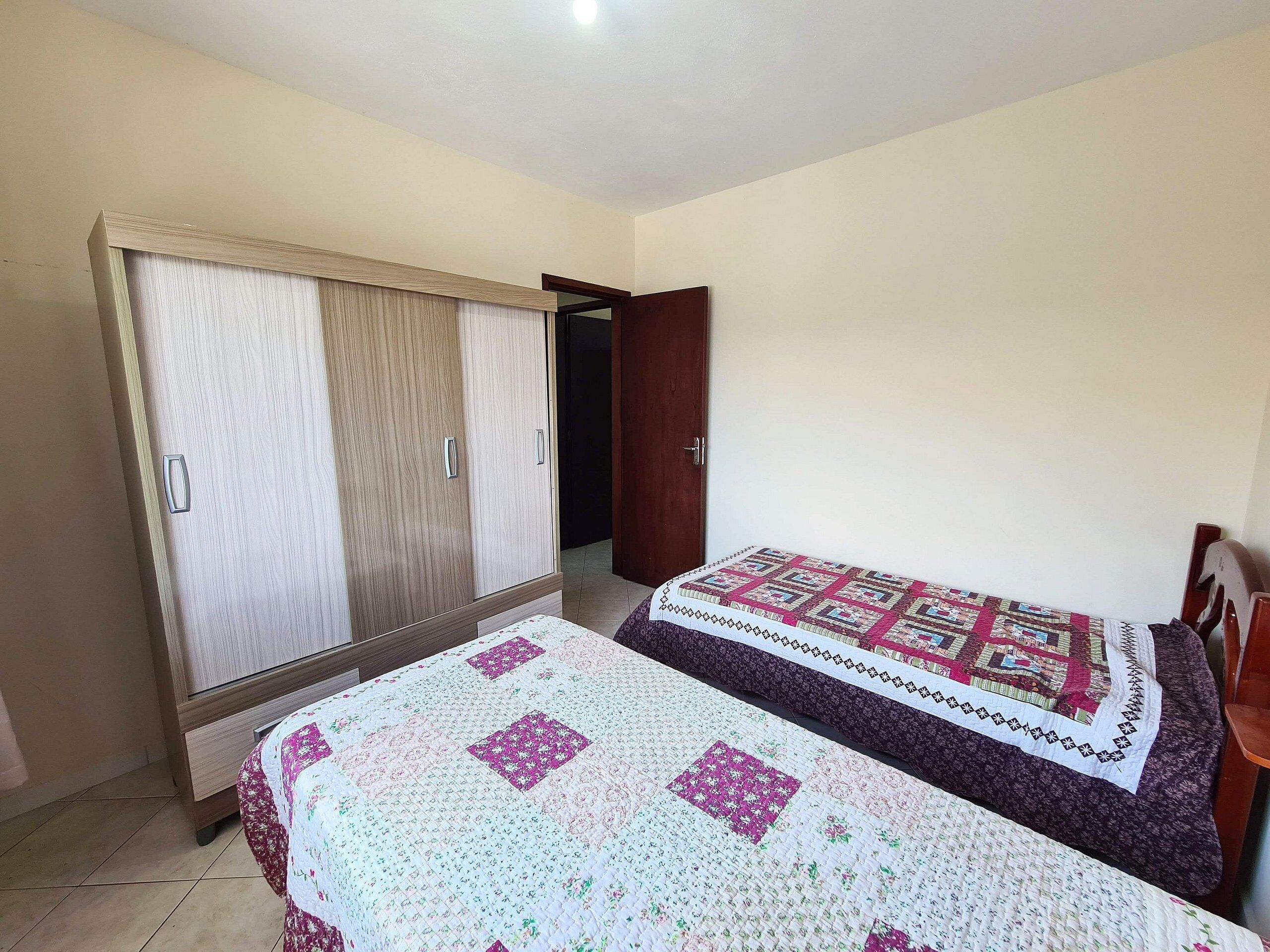 Um quarto com uma cama, um guarda-roupa e uma porta que dá para outro cômodo.