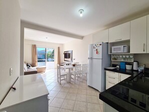 Eine moderne Küche mit Kühlschrank, Mikrowelle und Herd. Ein Essbereich mit Tisch und Stühlen lädt zum Verweilen ein, und im Hintergrund befindet sich eine Couch.