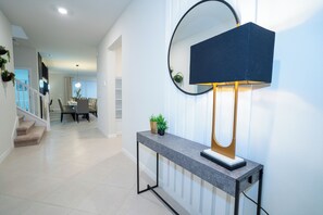 A modern hallway with a console table, a wall-mounted mirror, and a staircase leading to another room. - Special Offer! Near Disney/Themed BR/Pool/SPA 16276 (Clermont)