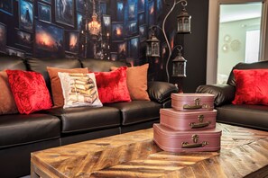 A living room with a black leather sofa, red and brown cushions, and a wooden coffee table with stacked pink suitcases. - Special Offer! Near Disney/Themed BR/Pool/SPA 16276 (Clermont)