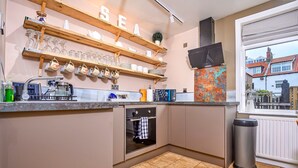 A kitchen with a built-in oven, a sink, and a window overlooking a residential area. - Whitby Coastal Cottage (Whitby)
