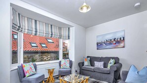 A cozy living room with a sofa, chairs, a glass coffee table, and a painting on the wall. - Whitby Coastal Cottage (Whitby)