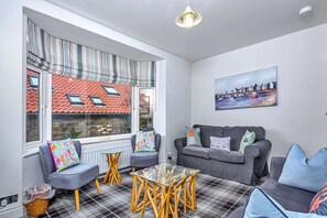 A cozy living room with a sofa, chairs, a glass coffee table, and a painting on the wall. - Whitby Coastal Cottage (Whitby)