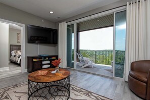 Ein modernes Wohnzimmer mit Flachbildfernseher, Couchtisch aus Holz und Blick auf einen Balkon mit Geländer.