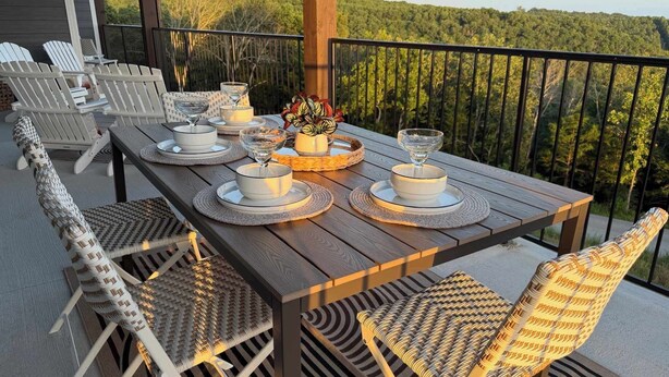 A wooden deck with a table set for dining, surrounded by wicker chairs, overlooking a forested landscape. - BWV 242 Nanna's Nook (Branson)