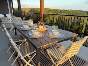 A wooden deck with a table set for dining, surrounded by wicker chairs, overlooking a forested landscape. - Nanna's Nook NEW Heated Indoor Pool Splashpad SDC (Branson)