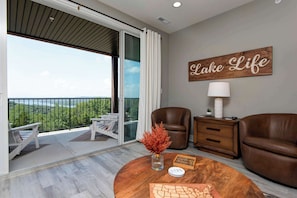 A modern living room with a view of a lake, a 'Lake Life' sign, a round wooden coffee table, and leather sofas. - Nanna's Nook NEW Heated Indoor Pool Splashpad SDC (Branson)