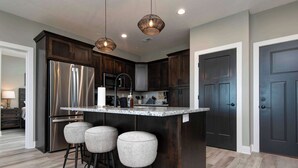A modern kitchen with dark wood cabinets, stainless steel appliances, a granite countertop, and a bar stool area. - BWV 242 Nanna's Nook (Branson)