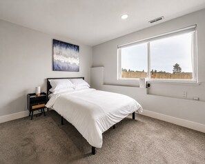 Ein Schlafzimmer mit einem Bett, einem Nachttisch, einer Wand-Klimaanlage und einem Fenster mit Blick auf einen Zaun und Bäume.